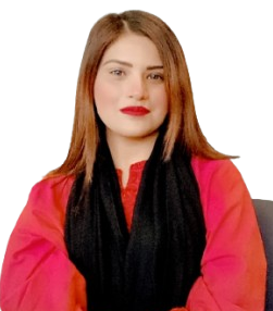 Woman with shoulder-length brown hair in a red outfit and black scarf sits at a table, hands folded, in a dining-like setting.